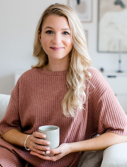 Health Coach Johanna Koch lächelnd auf dem Sofa in Hamburg mit Teetasse in der Hand